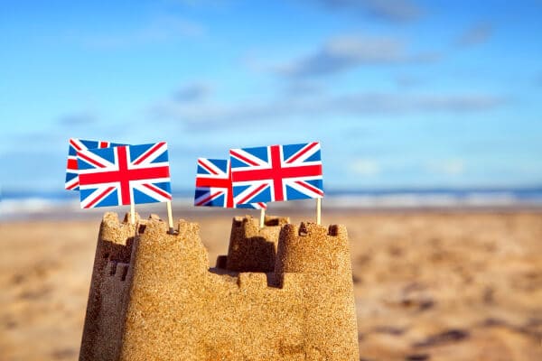 A sandcastle at the beach with british flags on the turrets.