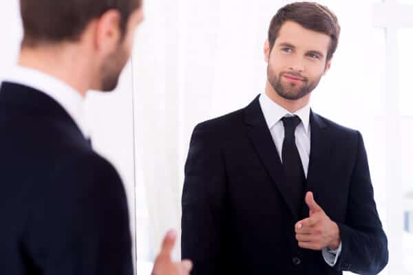 Self-care means recognising yourself. A man in a suit looking at himself in the mirror.