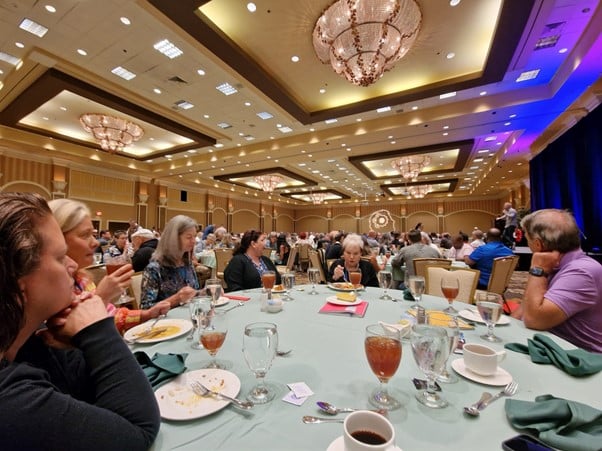 A picture showing the vastness of the ballroom where lunch is served every day, the closest table showing people eating. The ornate decor of the room is shown. 