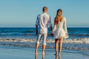 What is hypnotherapy used for? Improve relationships. A couple holding hands on a beach. 